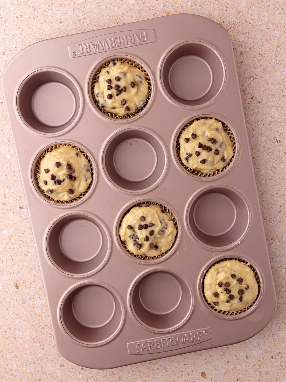 Chocolate chip banana muffin batter fills 5 wells in a muffin pan.