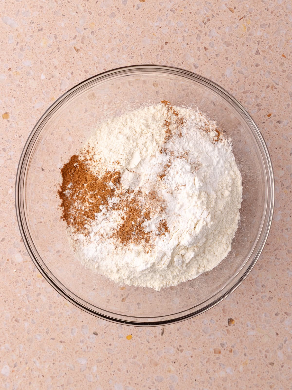 All-purpose flour, baking powder, baking soda, cinnamon and salt are in a glass mixing bowl.