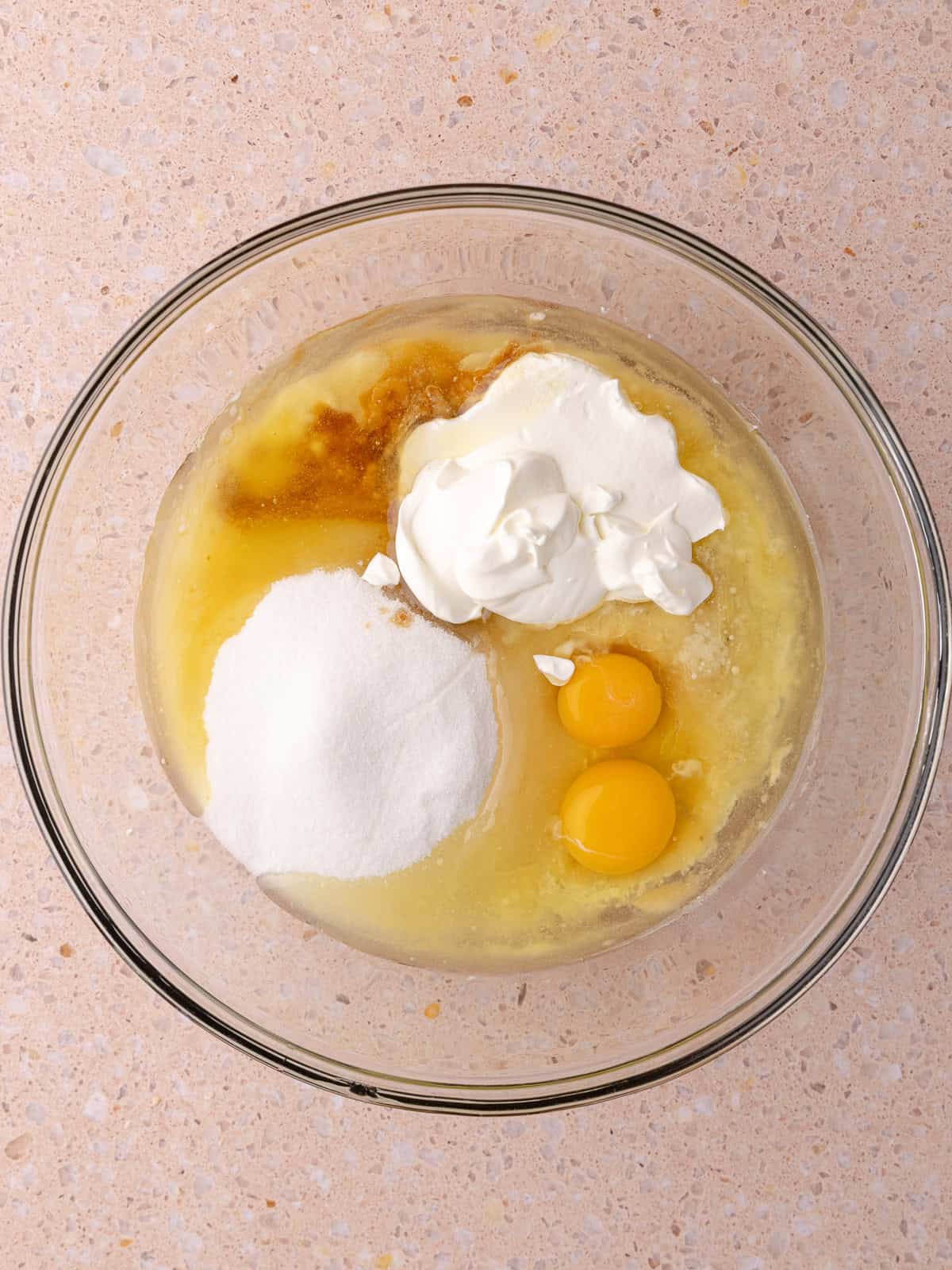 Mashed bananas, eggs, sugar, oil, melted butter, vanilla and sour cream are in a large mixing bowl.