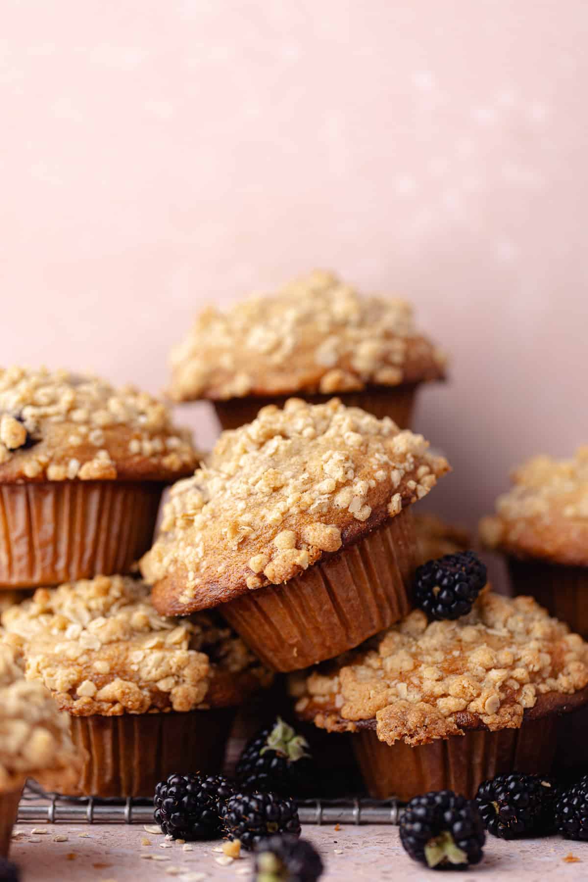 Banana blackberry oatmeal muffins with oatmeal streusel stacked on a wire rack with fresh blackberries.