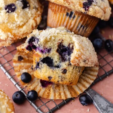 Bakery-style blueberry chocolate chip muffins with streusel topping sitting on a wire rack feature photo.