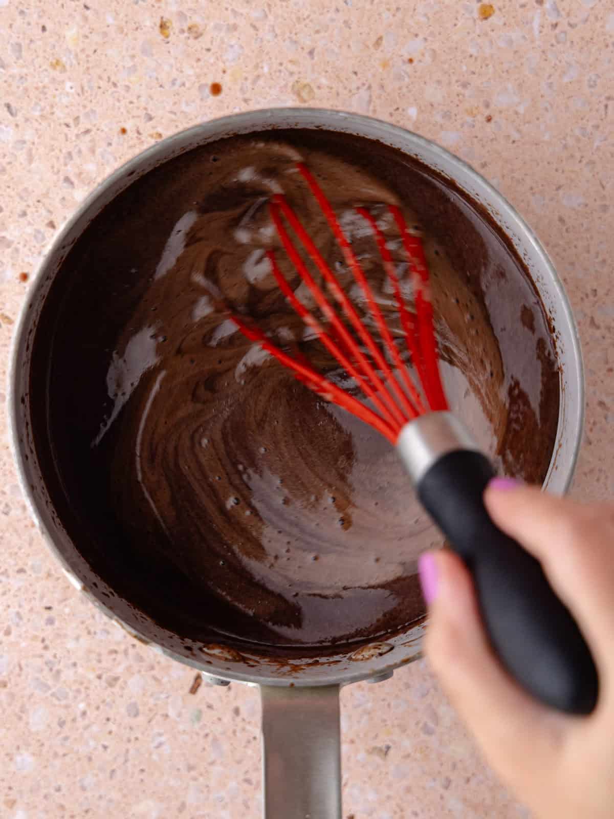 Chocolate chips are whisked into the chocolate ice cream base in a small saucepan.