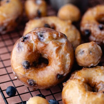 Glazed fried blueberry donuts sitting on a wire rack feature photo.