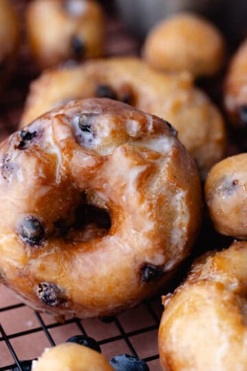 Glazed fried blueberry donuts sitting on a wire rack feature photo.