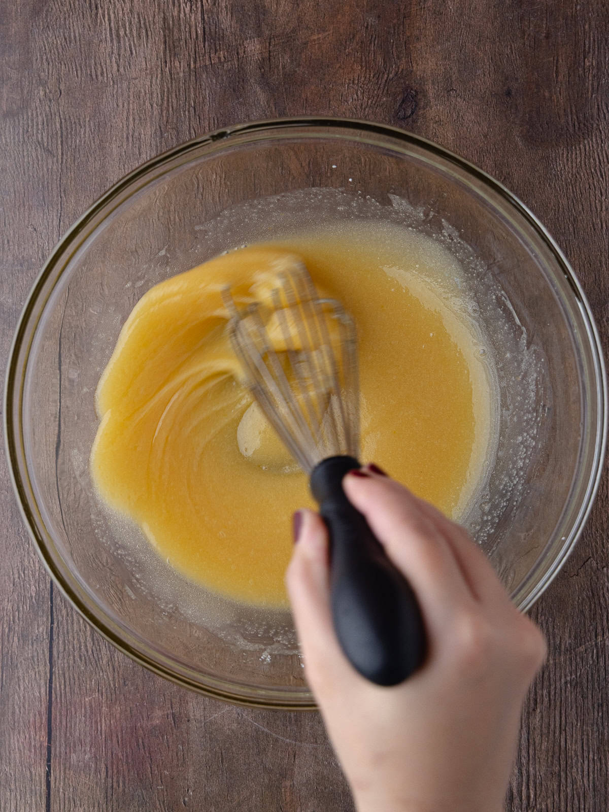 Wet ingredients are whisked together in a large glass mixing bowl.