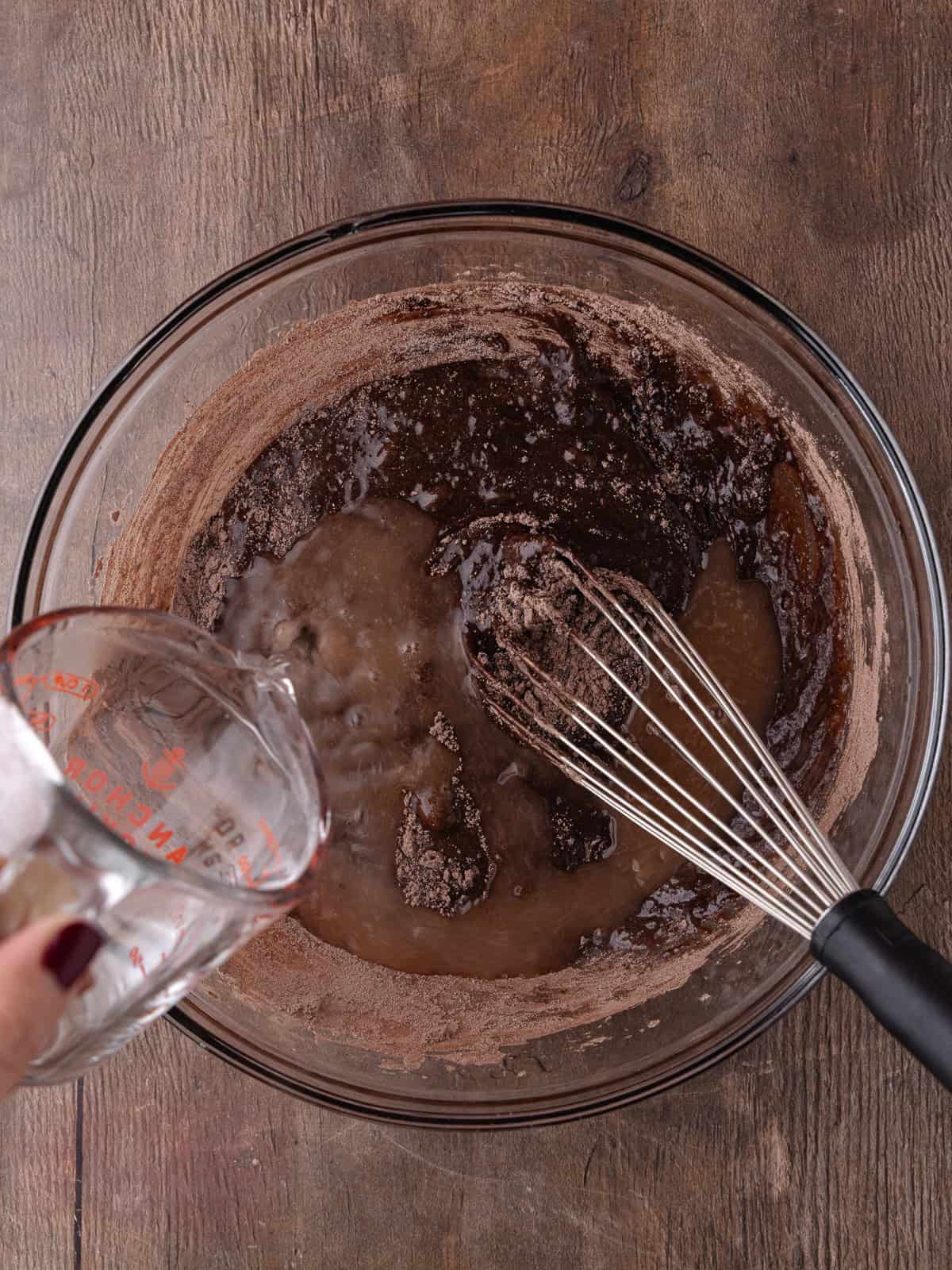 Hot water is added to the dark chocolate cake batter in a large glass bowl.