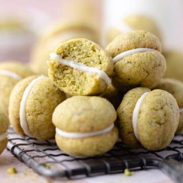 A pile of pistachio lemon sandwich cookies filled with white chocolate sitting on a wire rack featured photo.