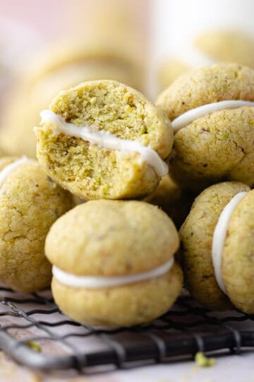 A pile of pistachio lemon sandwich cookies filled with white chocolate sitting on a wire rack featured photo.