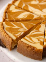 Pumpkin swirl cheesecake are cut into slices on a marble serving plate feature photo.