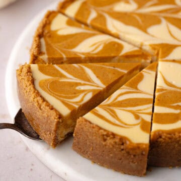 Pumpkin swirl cheesecake are cut into slices on a marble serving plate feature photo.