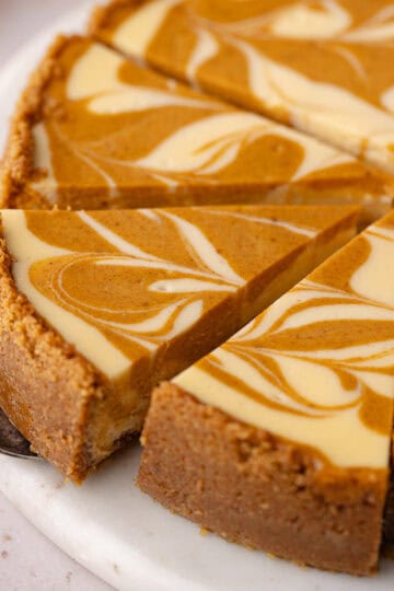 Pumpkin swirl cheesecake are cut into slices on a marble serving plate feature photo.