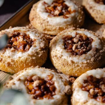 Apple cheesecake brioche buns filled with cheesecake filling, cinnamon apple pie filling and buttery streusel topping are sitting on a baking sheet feature photo.