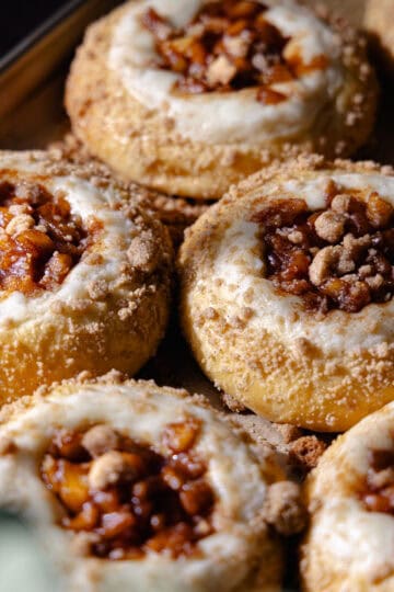 Apple cheesecake brioche buns filled with cheesecake filling, cinnamon apple pie filling and buttery streusel topping are sitting on a baking sheet feature photo.