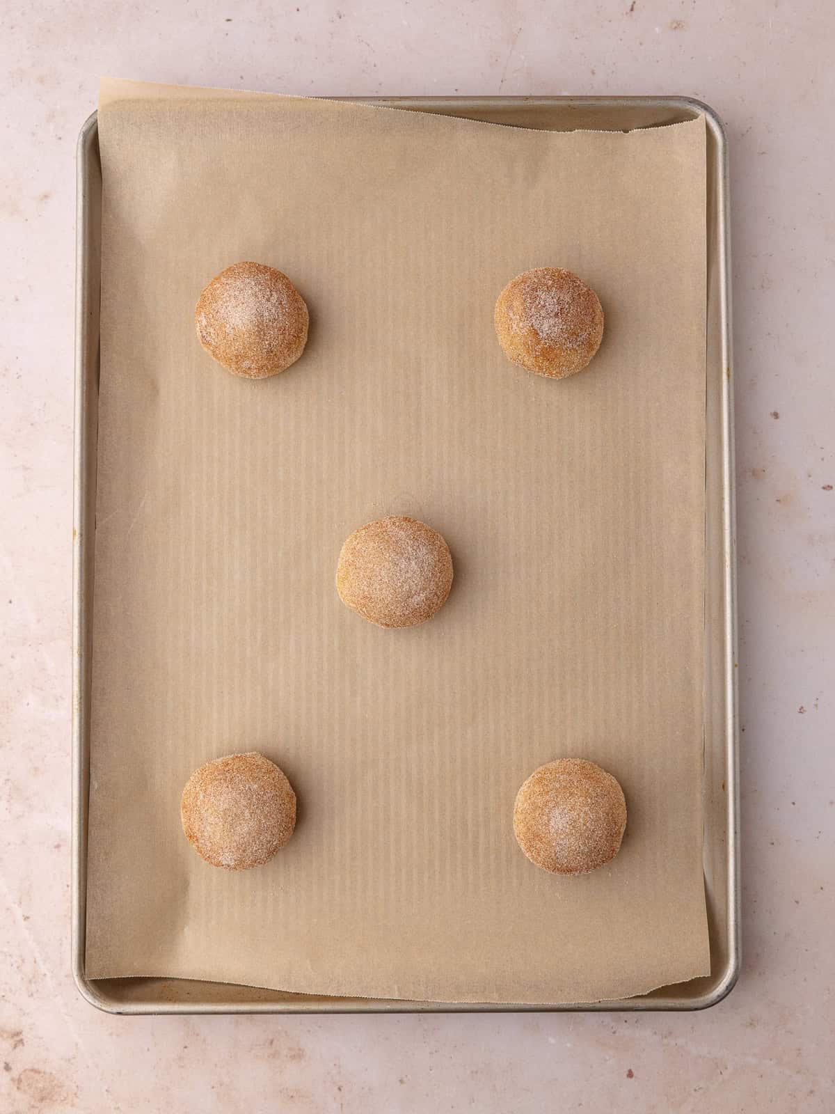 Gooey Biscoff stuffed snickerdoodle cookie dough balls are sitting on a baking sheet.