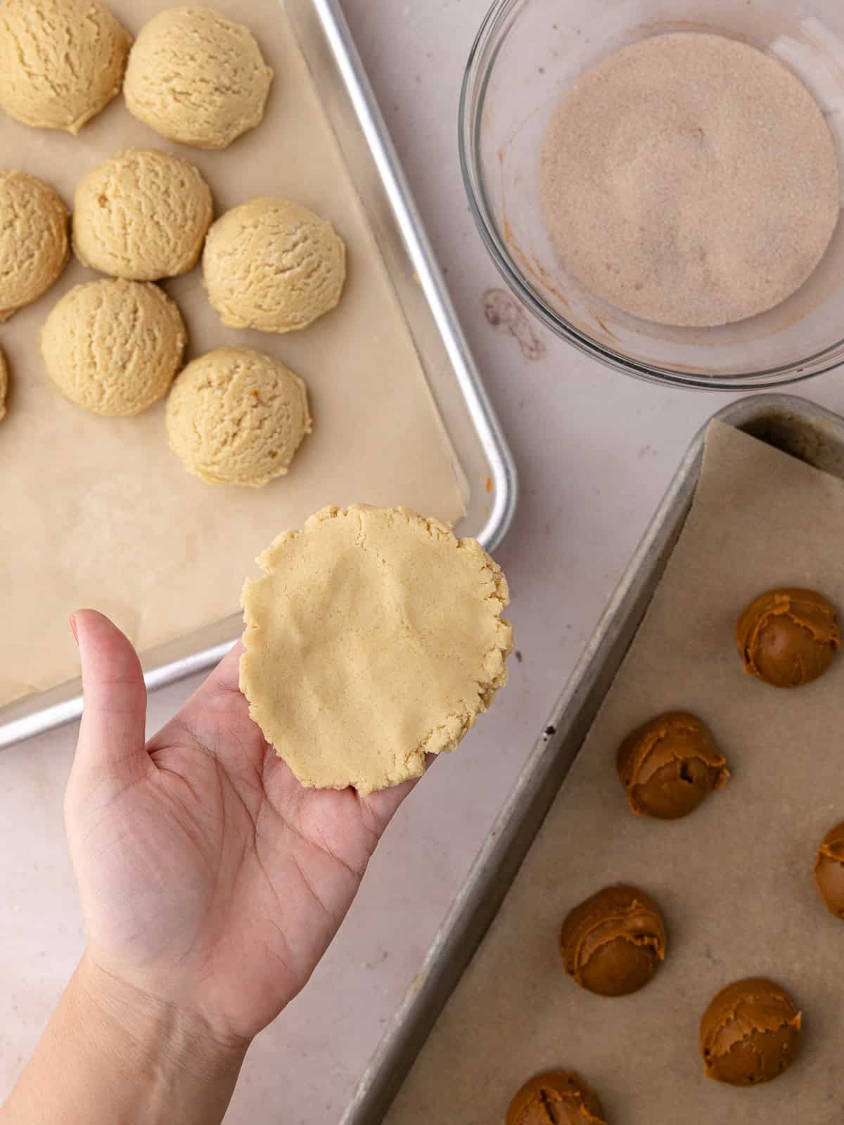 Snickerdoodle cookie dough balls are flattened in the palm of a hand.