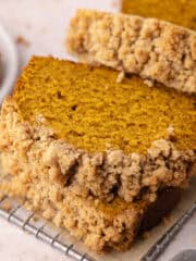 Moist and tender pumpkin bread with buttery cinnamon streusel topping is sliced and sitting on top of a small wire rack featured photo.