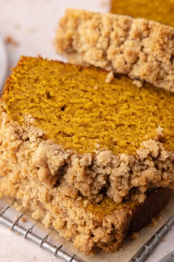 Moist and tender pumpkin bread with buttery cinnamon streusel topping is sliced and sitting on top of a small wire rack featured photo.