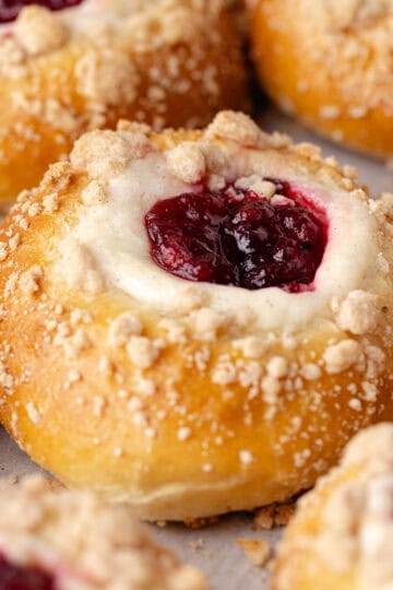 Cranberry cheesecake buns are made with a tangzhong milk bread dough, then filled with a vanilla cheesecake cream, cranberry orange jam and baked with a buttery cinnamon streusel topping featured photo.