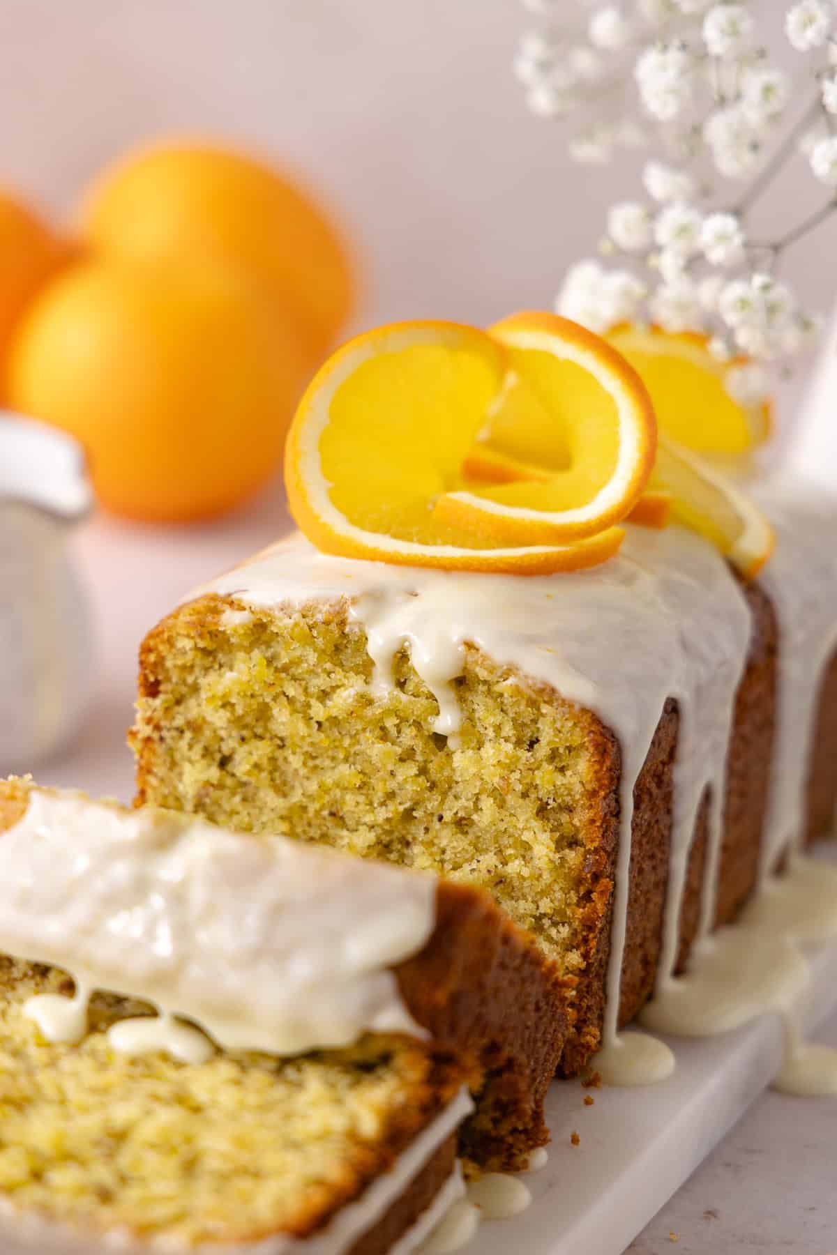 Pistachio Orange Olive Oil Cake topped with an orange glaze, is made with a whole orange and extra-virgin olive oil. Slices of Pistachio Orange Olive Oil Cake is sitting on a serving plate.
