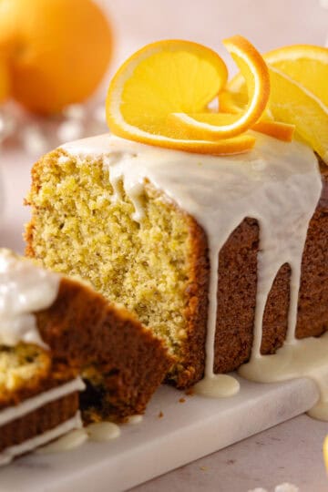 Pistachio orange cake topped with a fresh orange glaze is sliced and sitting on a serving platter feature photo.