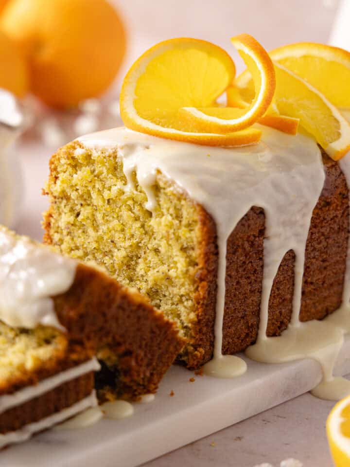 Pistachio orange cake topped with a fresh orange glaze is sliced and sitting on a serving platter feature photo.