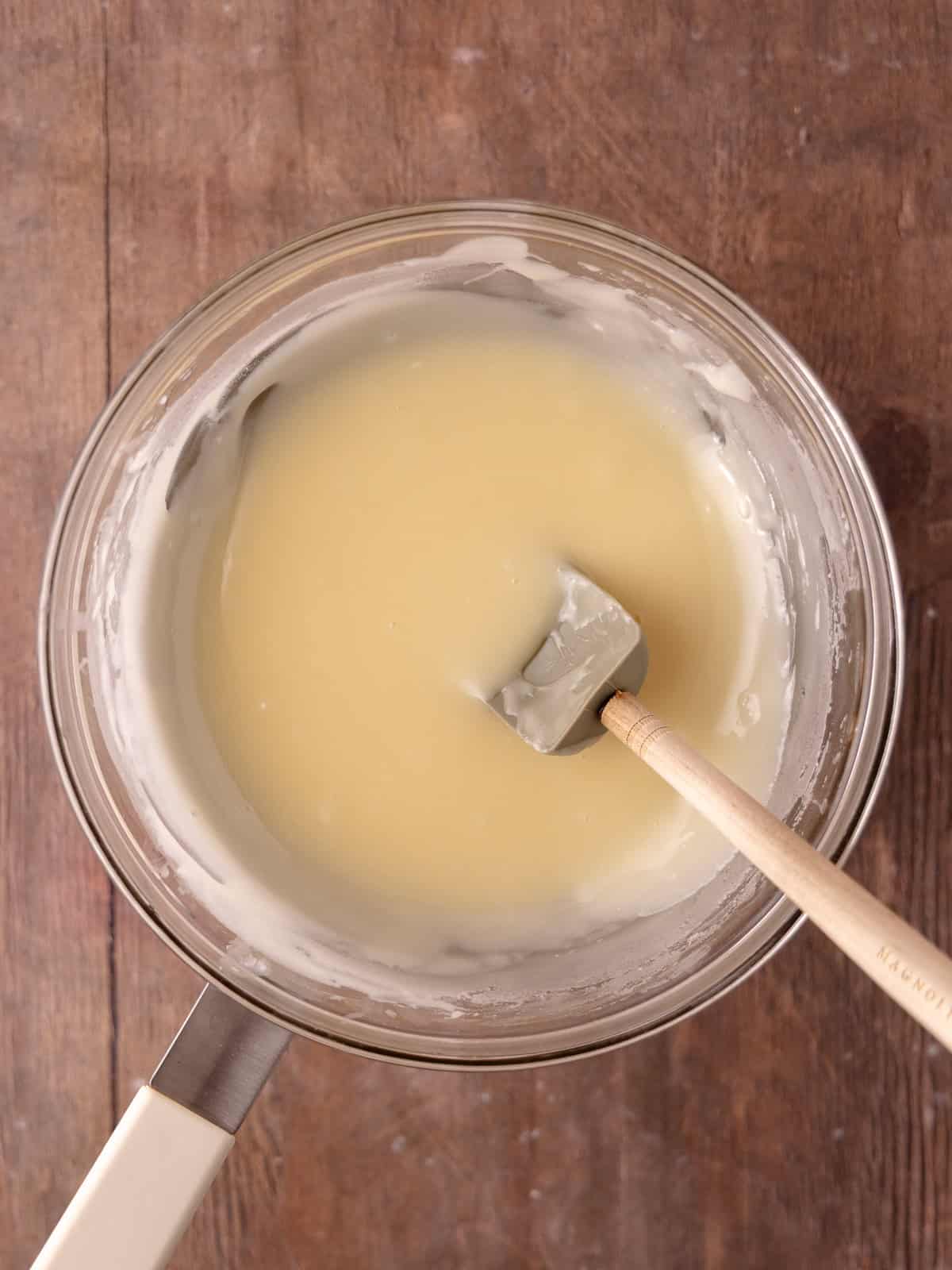 White chocolate and a bit of heavy cream is melted together in a heatproof bowl sitting over a pot of simmering water.