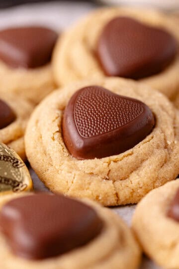 Super soft and moist peanut butter thumbprint cookies, also known as peanut butter blossom cookies are rolled in sugar and pressed with Reese's hearts peanut butter cups.