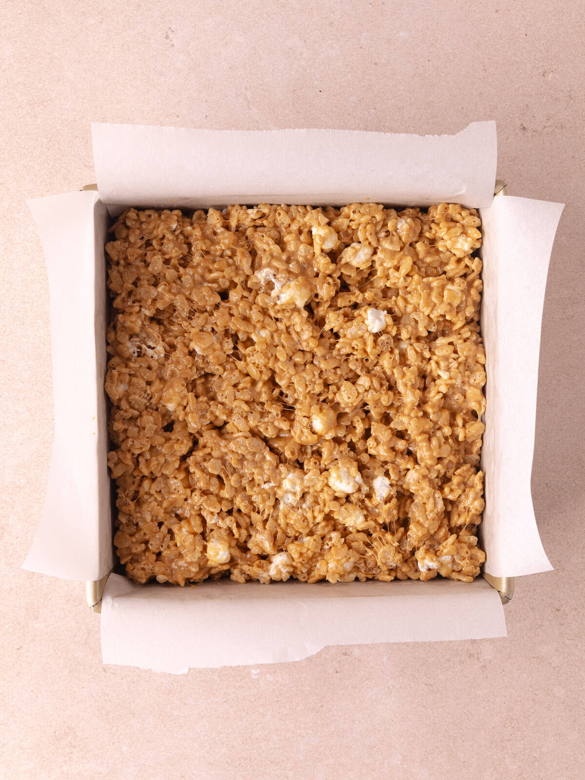 Biscoff rice krispie mixture is pressed into an 8x8 inch baking pan lined with parchment paper.
