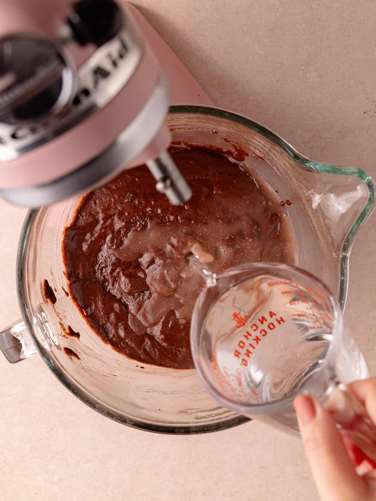 Hot water is poured into the bowl of a chocolate cake batter.