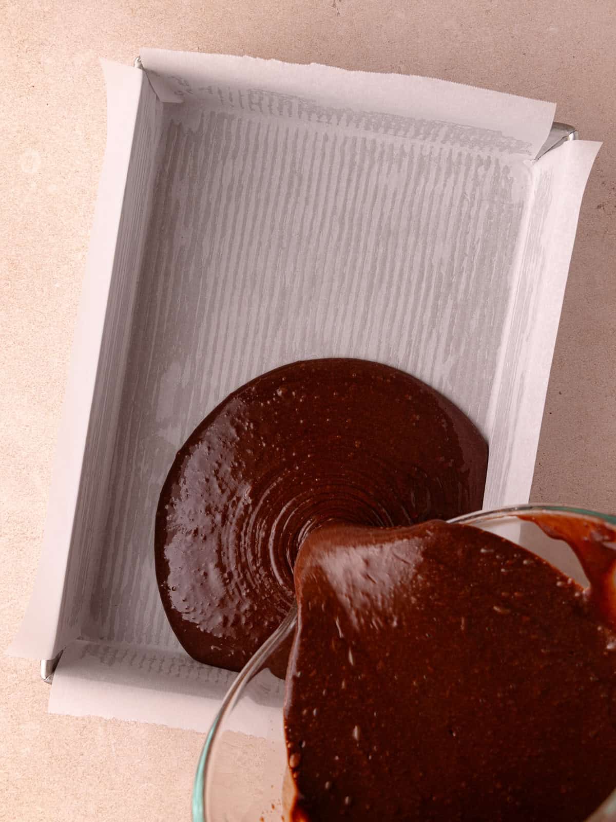 Chocolate malted cake batter is poured into a lined 9x13 inch baking pan.
