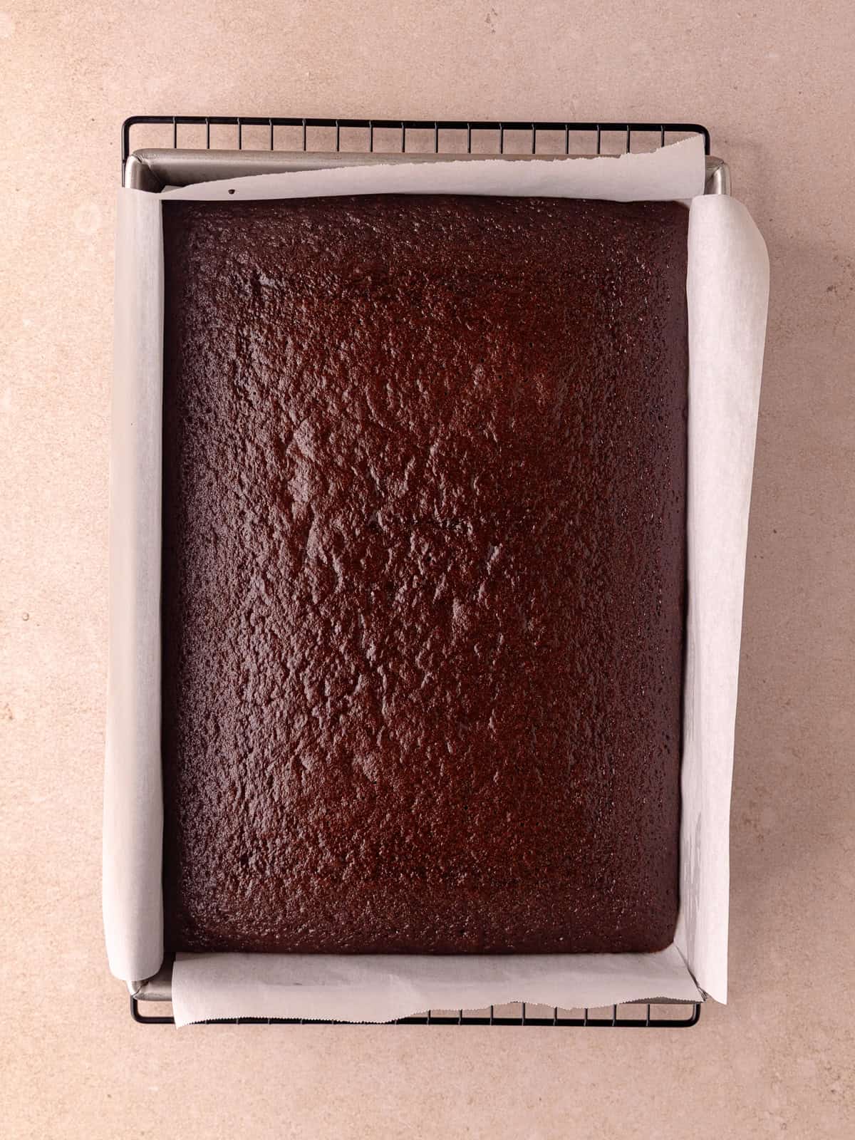 Chocolate malted cake is baked a 9x13 inch baking pan and sitting on a wire rack to cool.