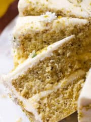 Slices of lemon pistachio cake frosted with cream cheese frosting on a cake plate.