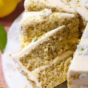 Slices of lemon pistachio cake frosted with cream cheese frosting on a cake plate.