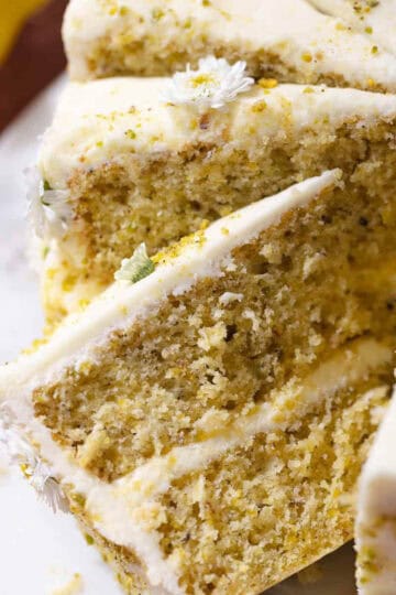 Slices of lemon pistachio cake frosted with cream cheese frosting on a cake plate.