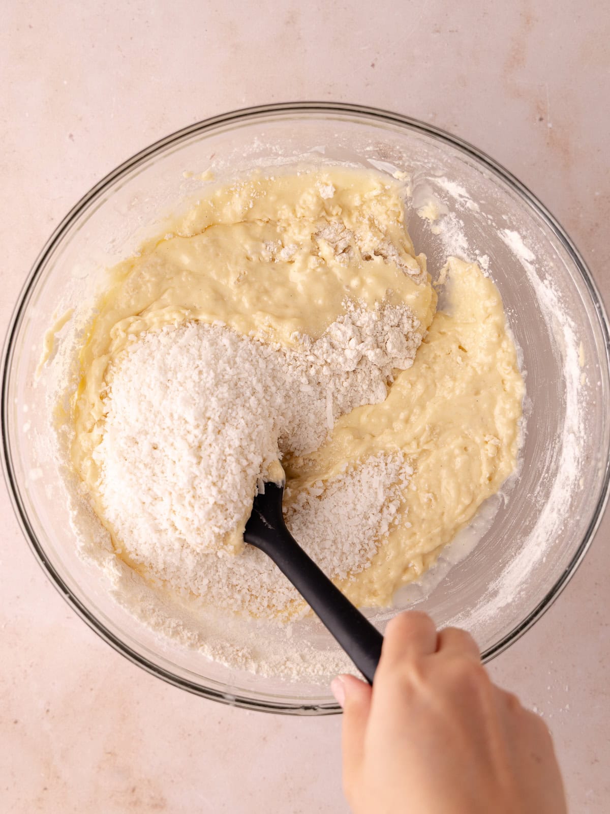 Shredded coconut is folded into the coconut cake batter in a large glass bowl.