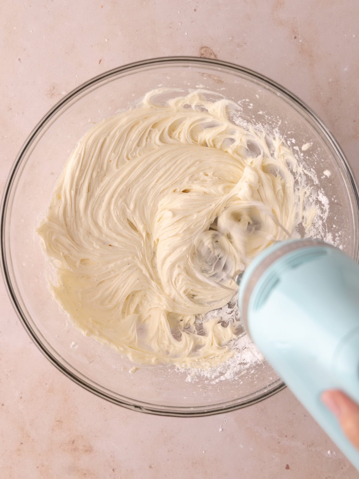 Cream cheese, powdered sugar, vanilla and coconut extract is whipped together in a large glass bowl.