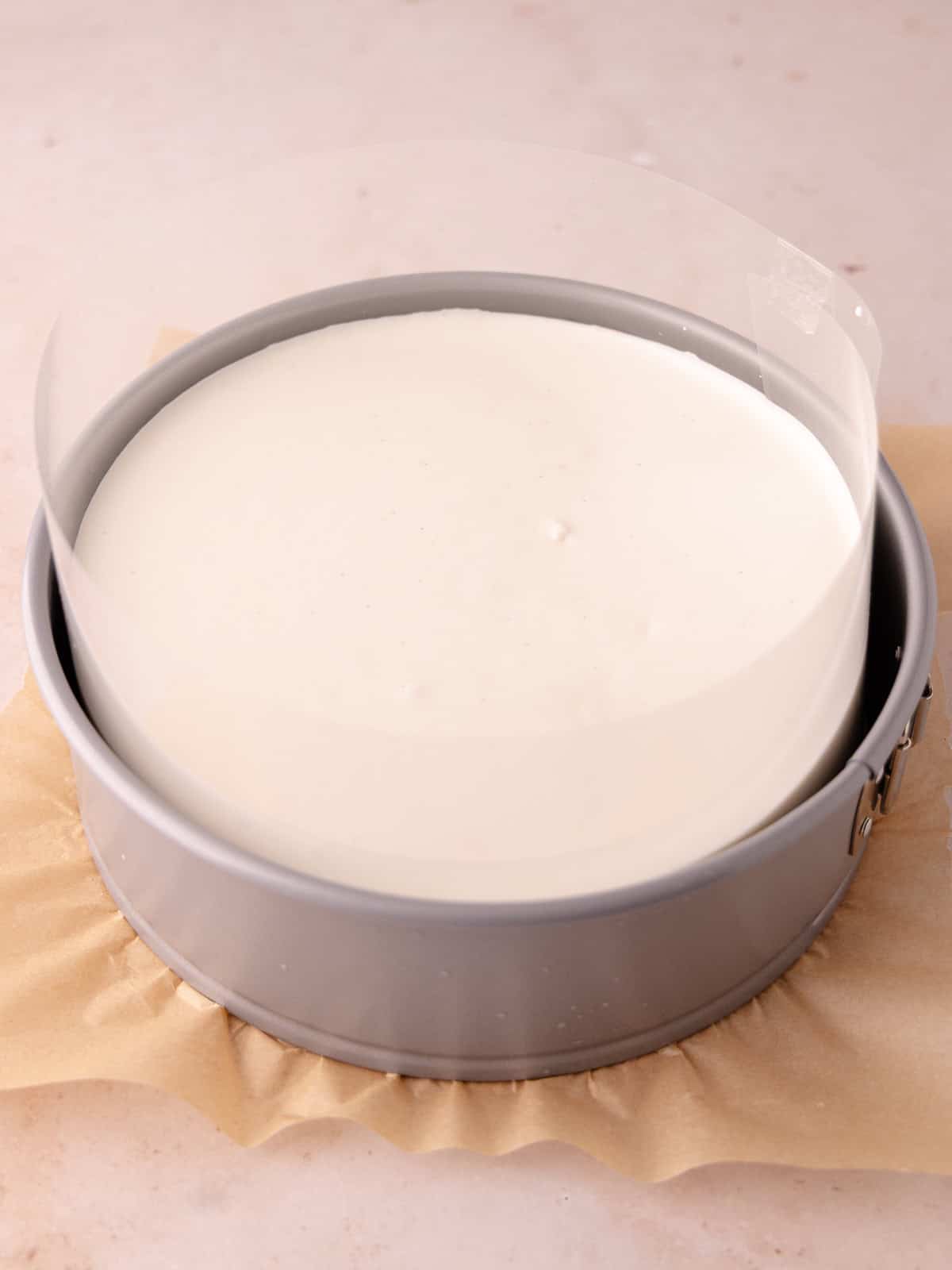 The coconut mousse layer is poured over the cooled coconut cake layer that's wrapped with a cake collar (acetate).