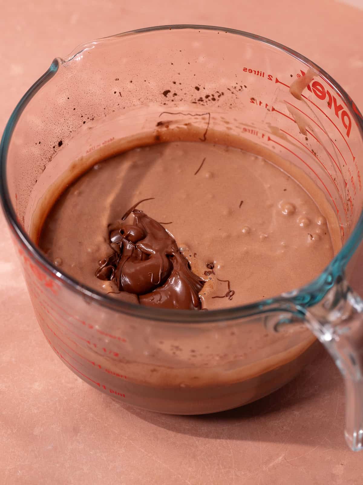 Melted chocolate is added to the chocolate coconut ice cream base that's sitting in a glass mixing bowl.