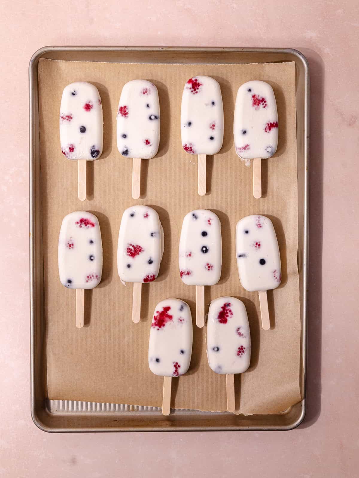 The creamy coconut popsicles are removed from the popsicle molds and placed on a large baking sheet lined with parchment paper.
