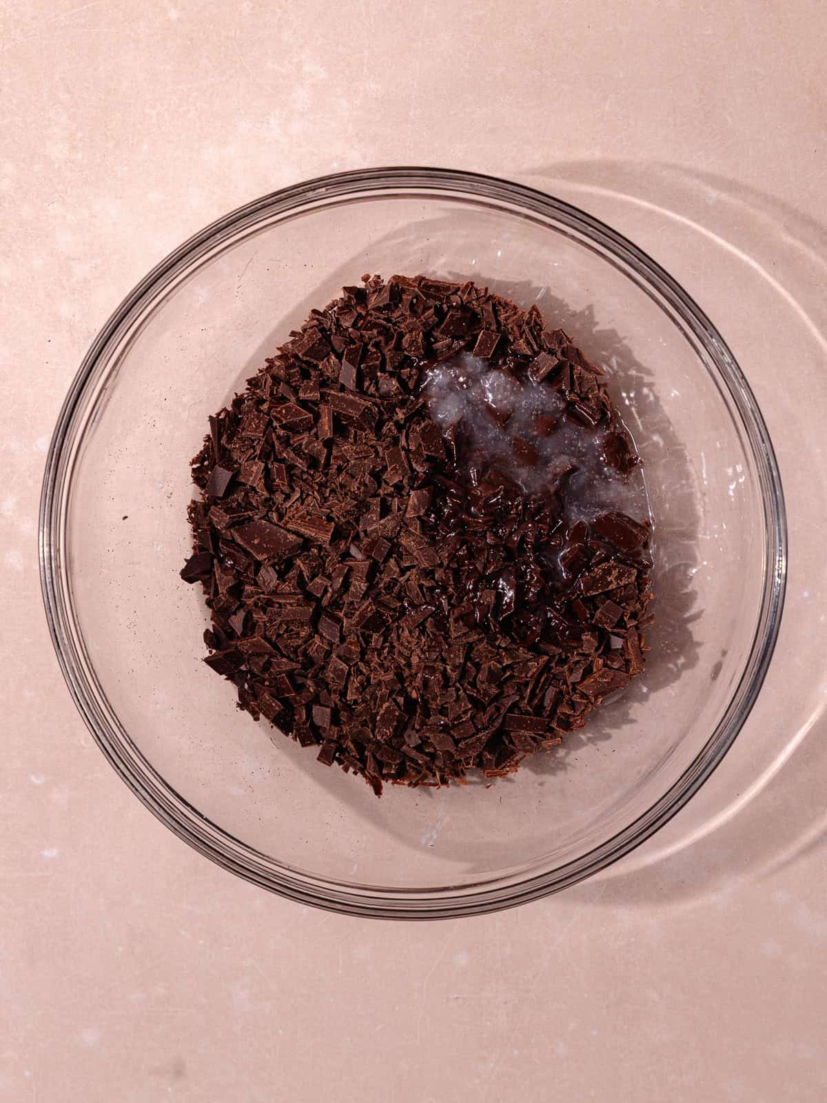 Finely chopped chocolate and coconut oil is in a medium glass bowl.