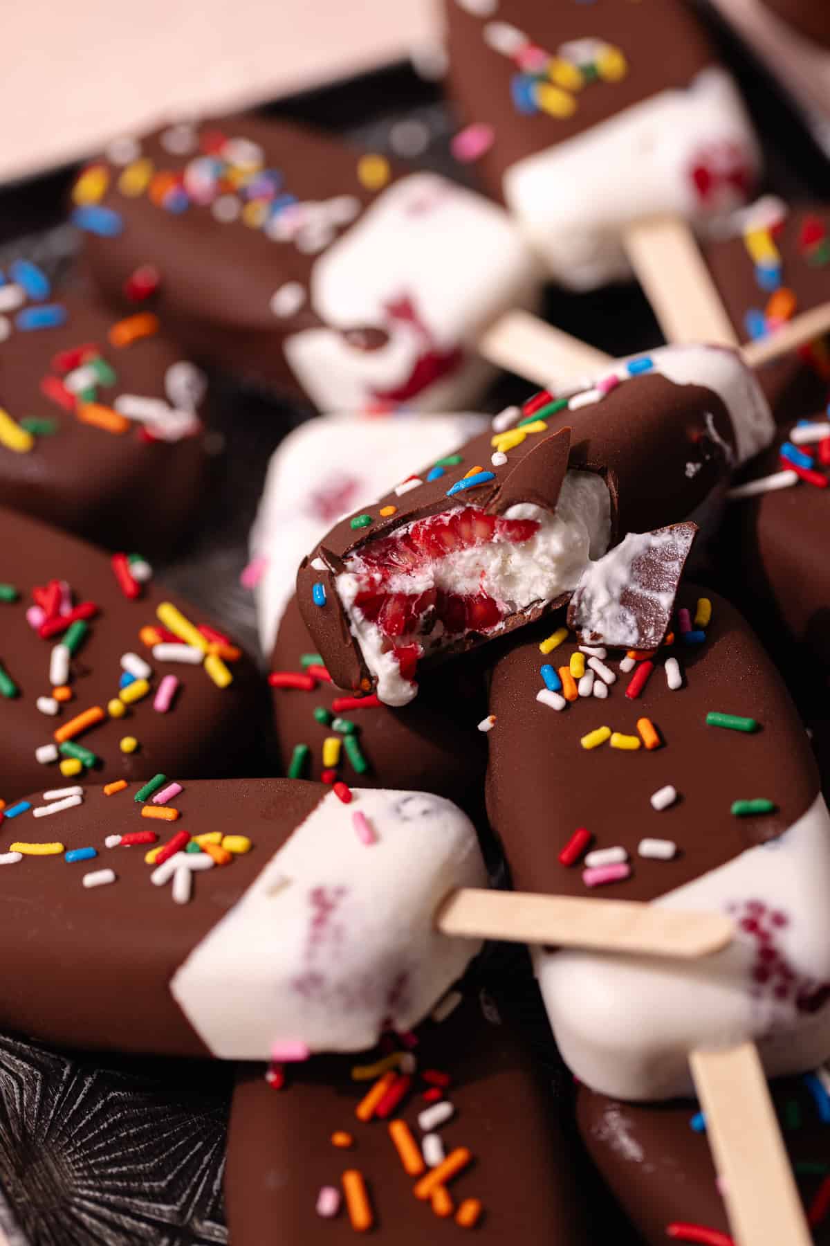 Creamy coconut popsicles with fresh raspberries and blueberries are dipped in a magic chocolate shell and topped with rainbow sprinkles.