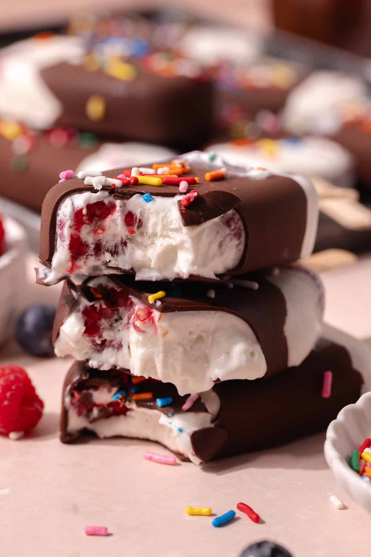 Creamy coconut popsicles with fresh raspberries and blueberries are dipped in a magic chocolate shell and topped with rainbow sprinkles.