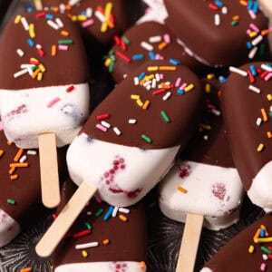 Creamy coconut popsicles with fresh raspberries and blueberries are dipped in a magic chocolate shell and topped with rainbow sprinkles.