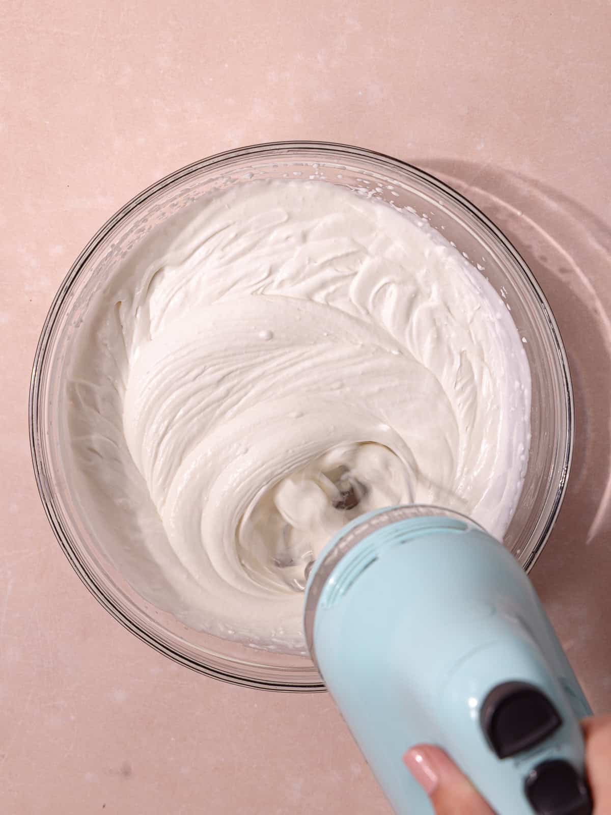 Coconut cream, cold heavy cream, sweetened condensed milk and coconut extract are whisked together in a glass mixing bowl until thick and creamy.
