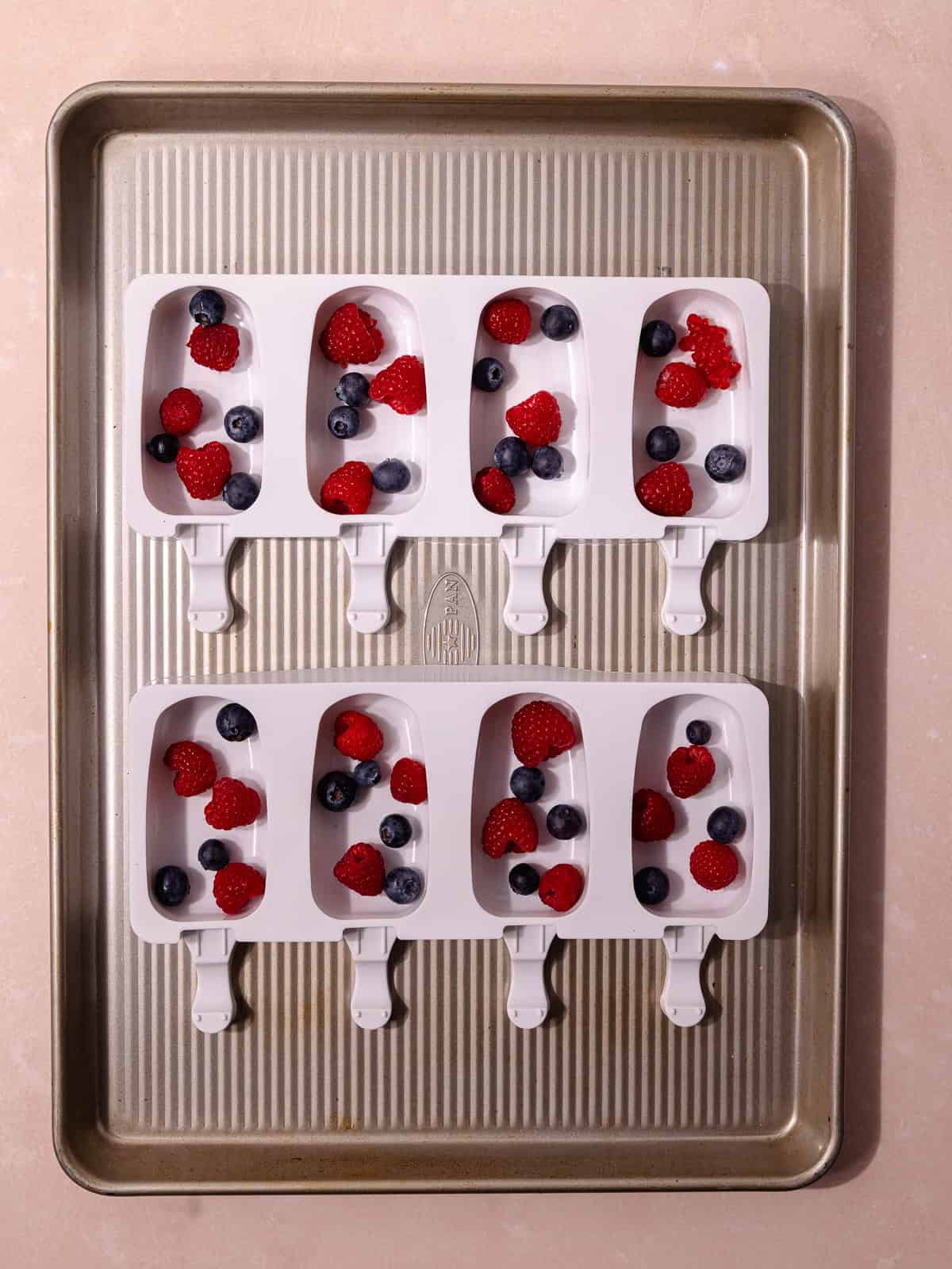Fresh blueberries and fresh raspberries are added to popsicle molds.