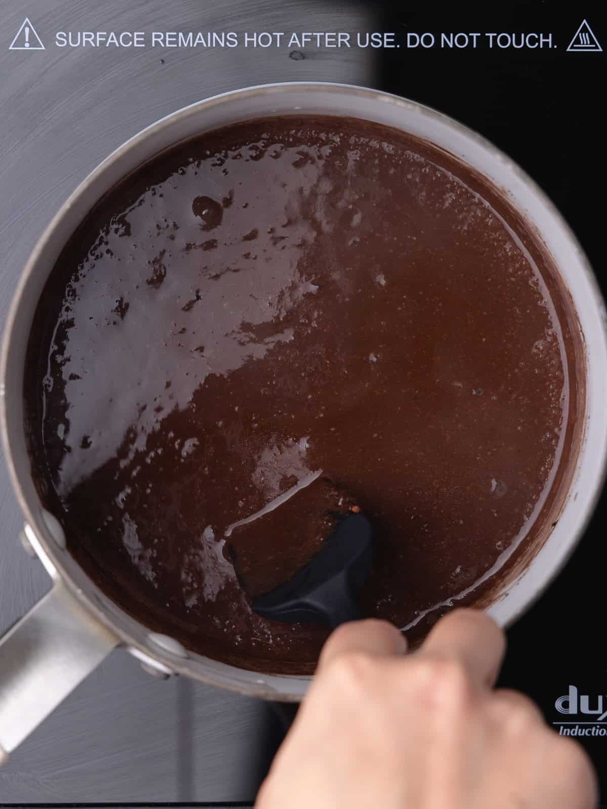 A saucepan with whole milk, cocoa powder, cubed unsalted butter, and salt are cooked over low heat until melted and combined.
