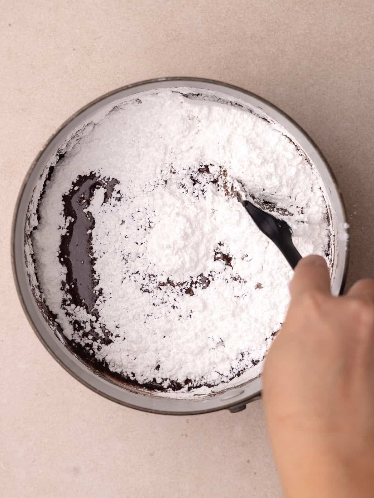 Powdered sugar is mixed into the pot of chocolate icing until smooth.
