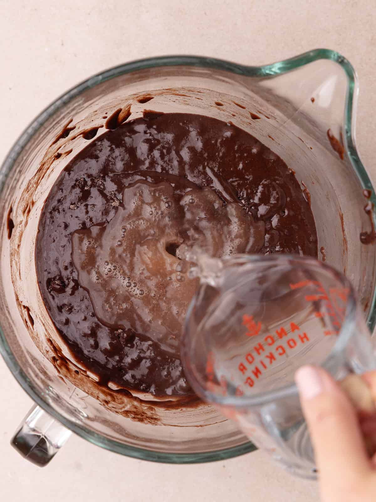 Hot water is poured into the bowl of a chocolate cake batter.