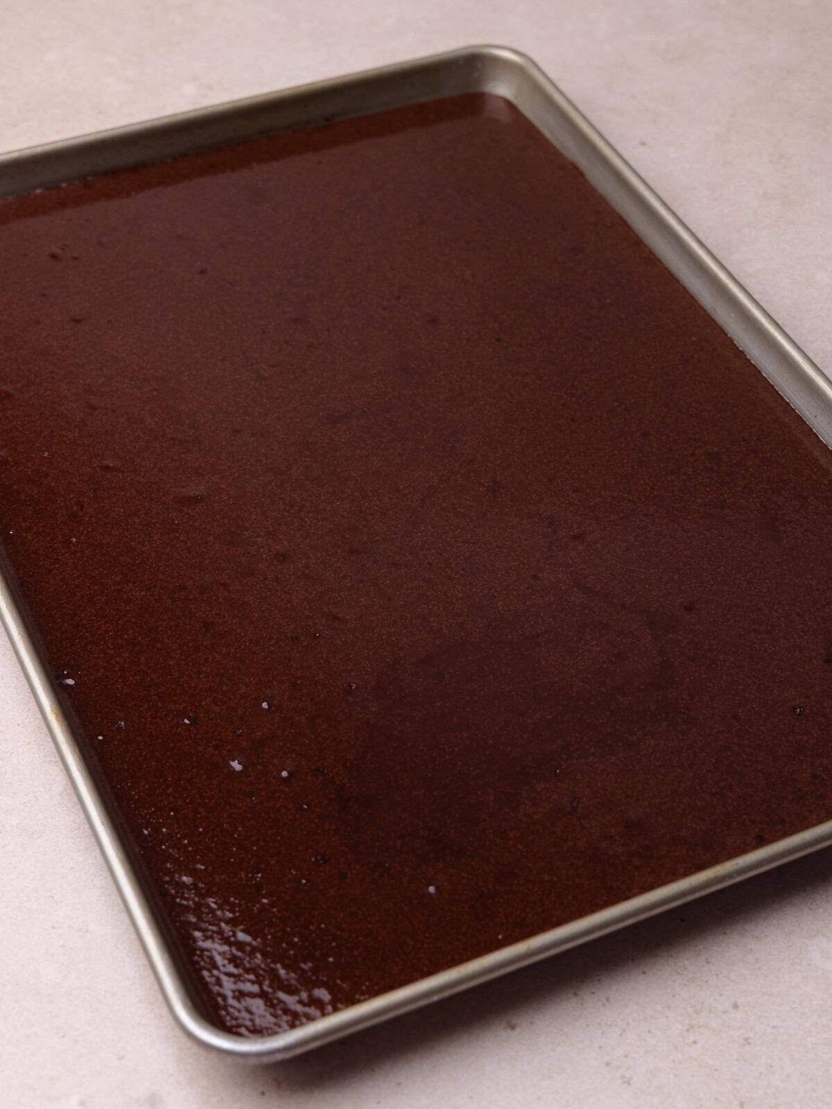 The dark chocolate cake batter is poured into a greased sheet pan, as known as a half sheet pan.