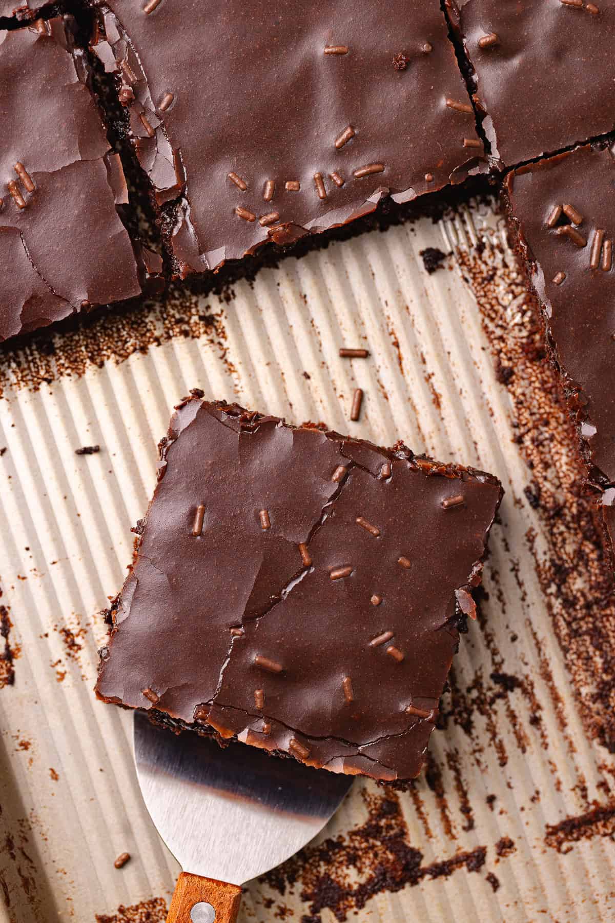 Dark chocolate sheet cake, also known as Texas sheet cake, is topped with a dark chocolate icing and chocolate sprinkles, and cut into squares.